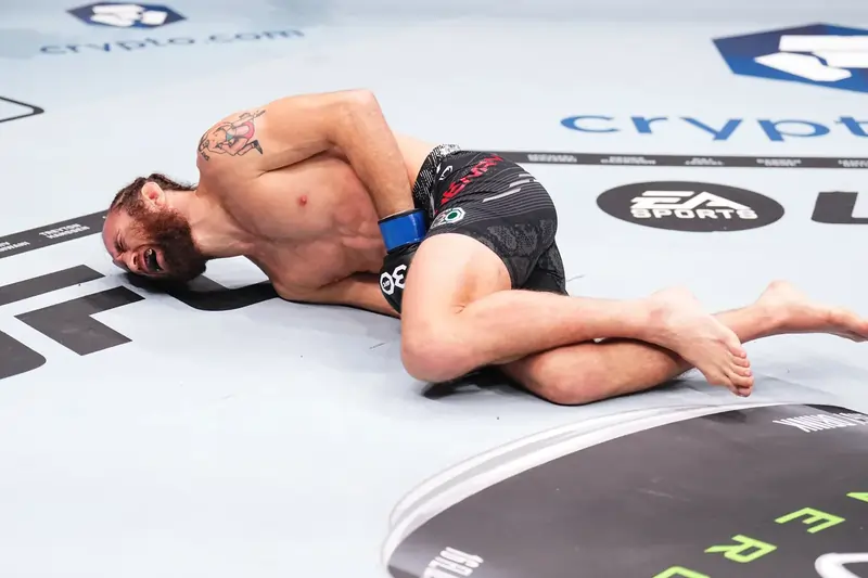 A UFC fighter (right) winces in pain after a low blow kick lands (left) during a fight. Even with a cup, accidental groin strikes can cause significant pain and halt the action. Do UFC Fighters Wear a Cup?